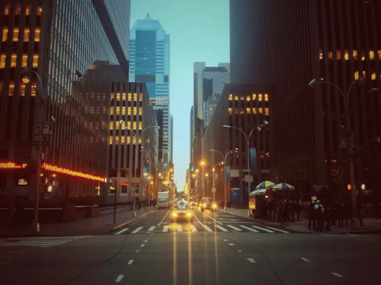 Front shot of a yellow taxi driving through nighttime New York City traffic.